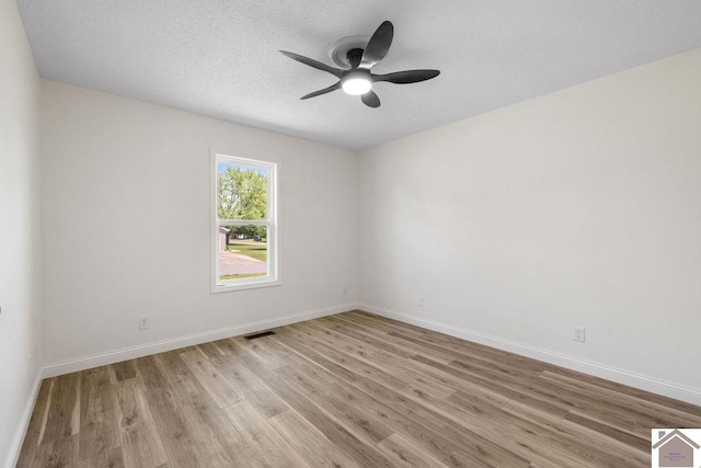spare room featuring baseboards, ceiling fan, wood finished floors, and visible vents