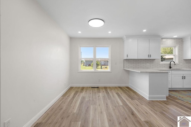 kitchen with white cabinetry, tasteful backsplash, a sink, and light wood-type flooring