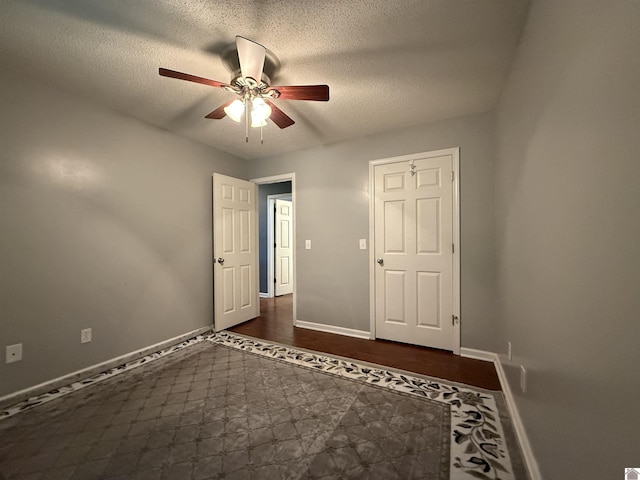unfurnished bedroom featuring a textured ceiling, baseboards, dark wood-style floors, and ceiling fan