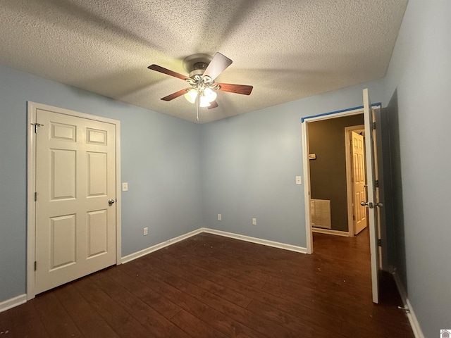 empty room featuring a textured ceiling, ceiling fan, baseboards, and dark wood-type flooring