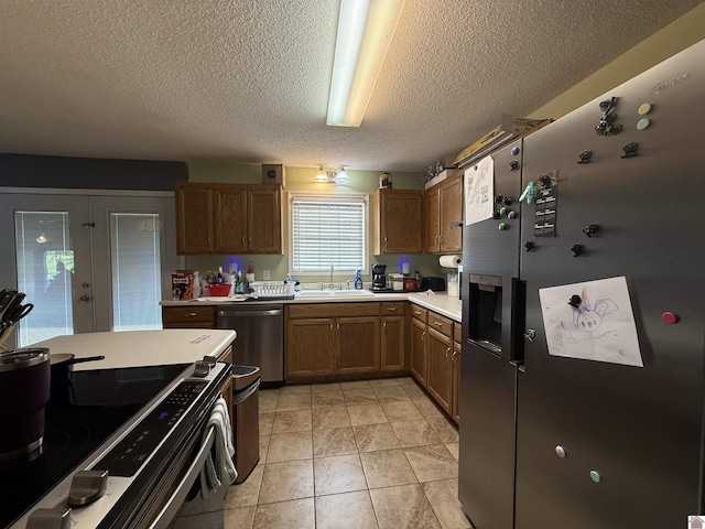 kitchen featuring appliances with stainless steel finishes, a sink, light countertops, a textured ceiling, and brown cabinetry