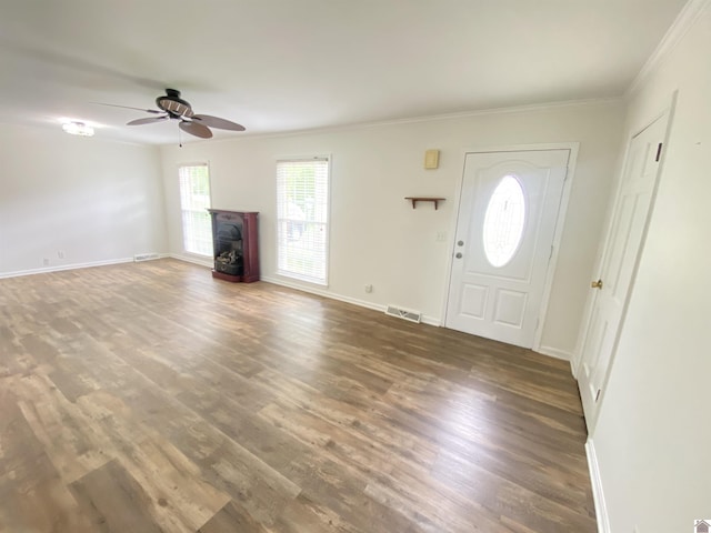unfurnished living room featuring visible vents, a wood stove, crown molding, wood finished floors, and ceiling fan