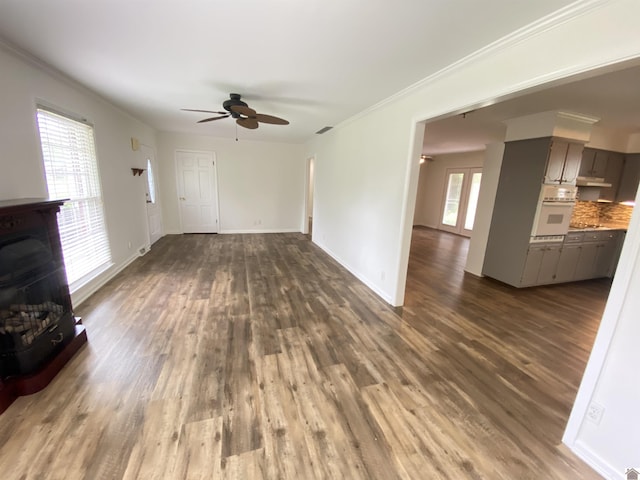 unfurnished living room featuring crown molding, ceiling fan, a fireplace, and dark wood-type flooring
