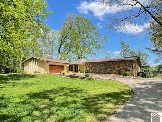 view of front of property featuring stone siding, an attached garage, driveway, and a front yard