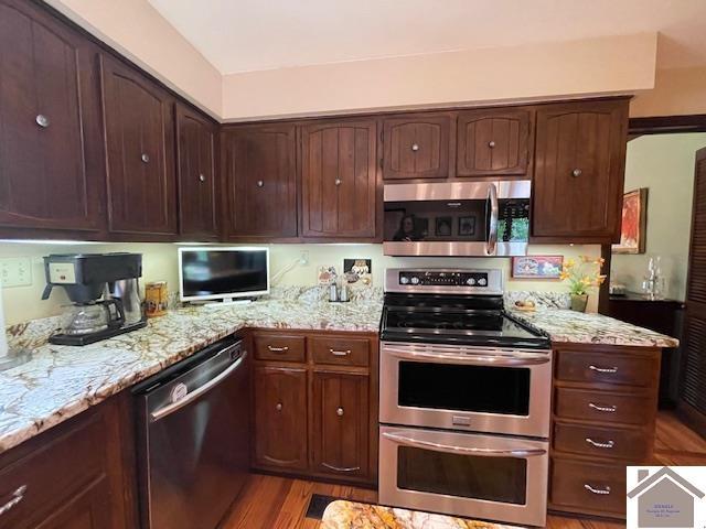 kitchen featuring stainless steel appliances, dark brown cabinetry, light stone counters, and light wood-style flooring