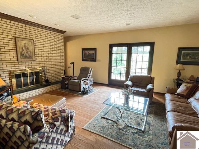 living area featuring a brick fireplace, a textured ceiling, baseboards, and wood finished floors