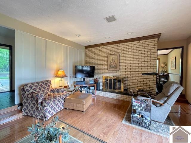 living room with a brick fireplace, a textured ceiling, and wood finished floors