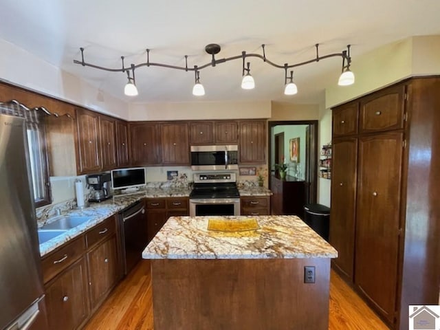 kitchen with light wood-style floors, appliances with stainless steel finishes, a center island, and light stone counters