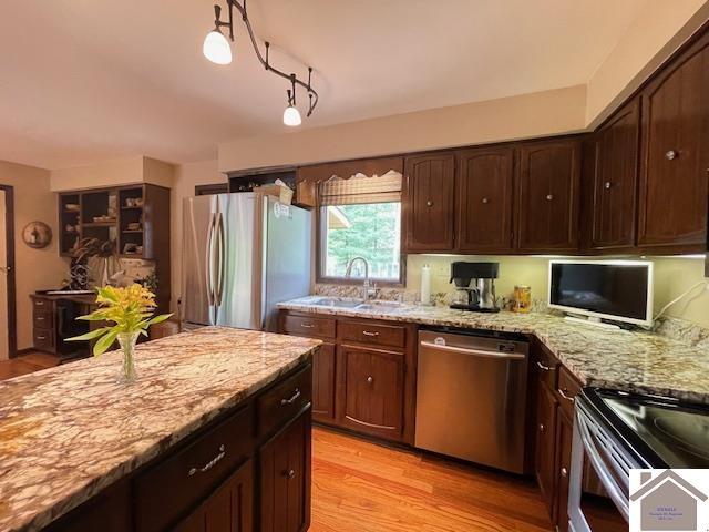 kitchen with dark brown cabinetry, light stone countertops, a sink, light wood-style flooring, and stainless steel appliances