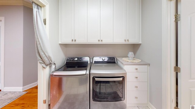 washroom featuring washing machine and clothes dryer, baseboards, light wood-style flooring, and cabinet space