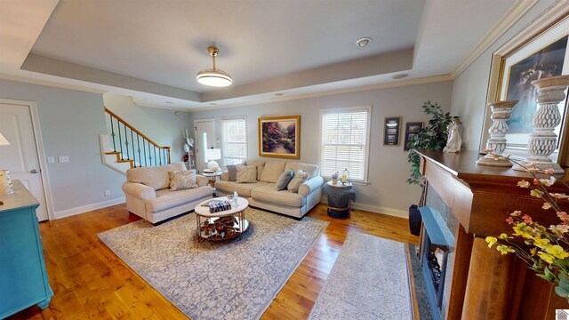living room with a fireplace, baseboards, light wood finished floors, a tray ceiling, and stairs