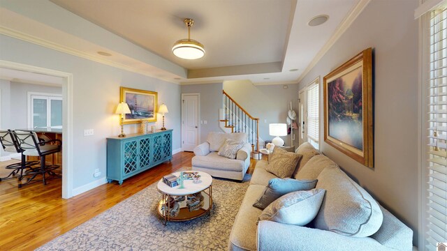 living area with baseboards, wood finished floors, a tray ceiling, ornamental molding, and stairway