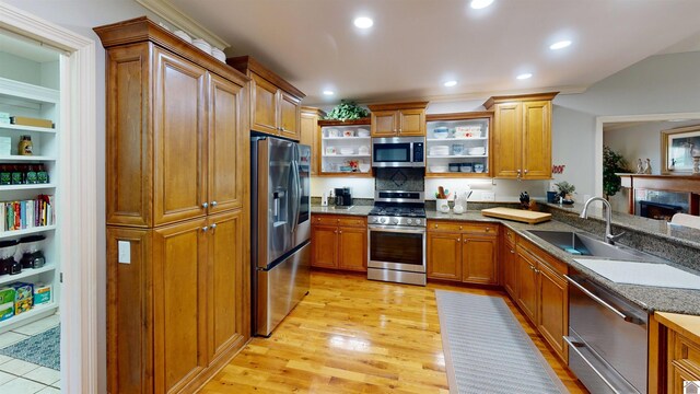 kitchen with appliances with stainless steel finishes, open shelves, brown cabinets, light wood-type flooring, and a sink