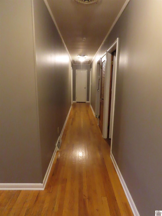 corridor featuring crown molding, baseboards, and light wood-type flooring
