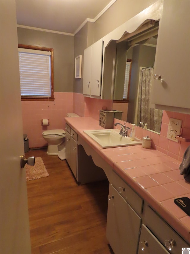 full bath featuring crown molding, tile walls, wood finished floors, a wainscoted wall, and toilet