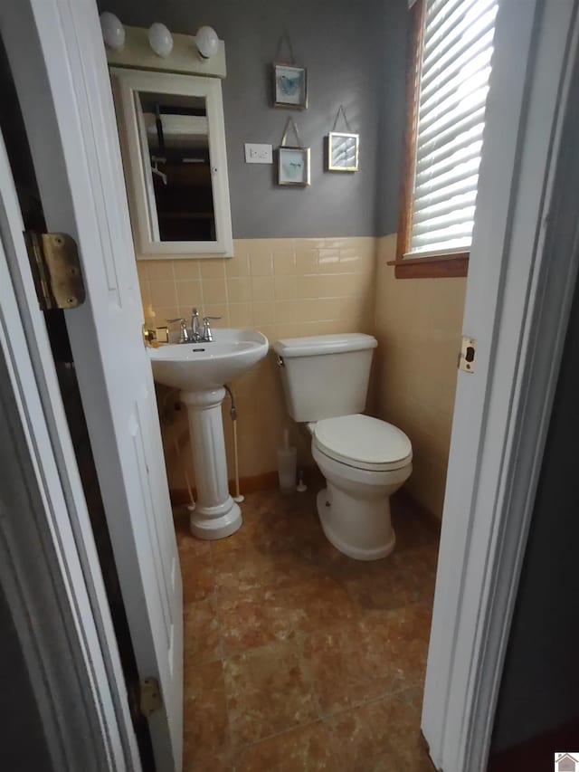 half bathroom featuring a sink, tile walls, and toilet