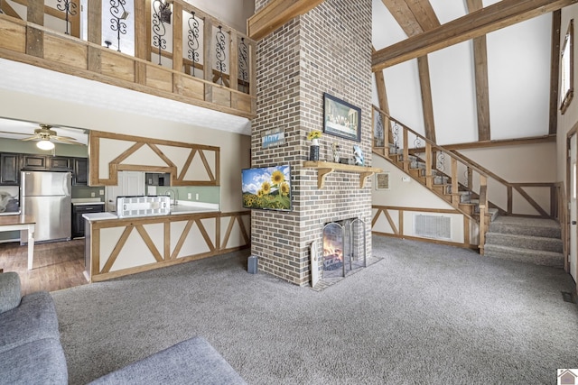living area featuring a ceiling fan, a brick fireplace, stairway, a high ceiling, and carpet