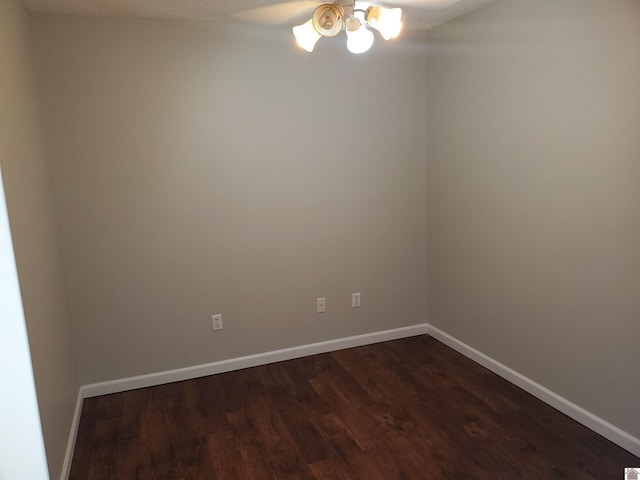 spare room featuring ceiling fan, dark wood finished floors, and baseboards