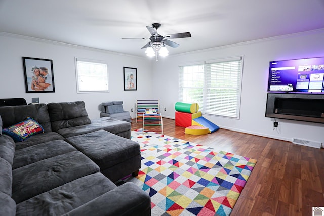 living area with baseboards, ornamental molding, visible vents, ceiling fan, and wood finished floors