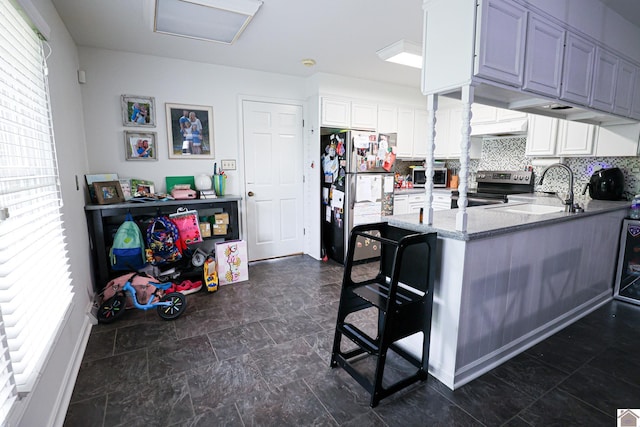 kitchen featuring a peninsula, a kitchen bar, a sink, stainless steel appliances, and light stone countertops