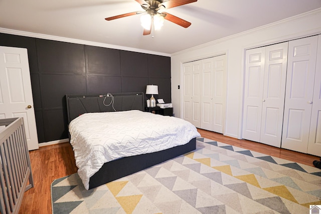 bedroom with ornamental molding, light wood-type flooring, a decorative wall, and two closets