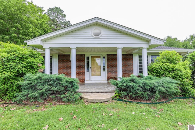 neoclassical / greek revival house with a porch, brick siding, and a front lawn