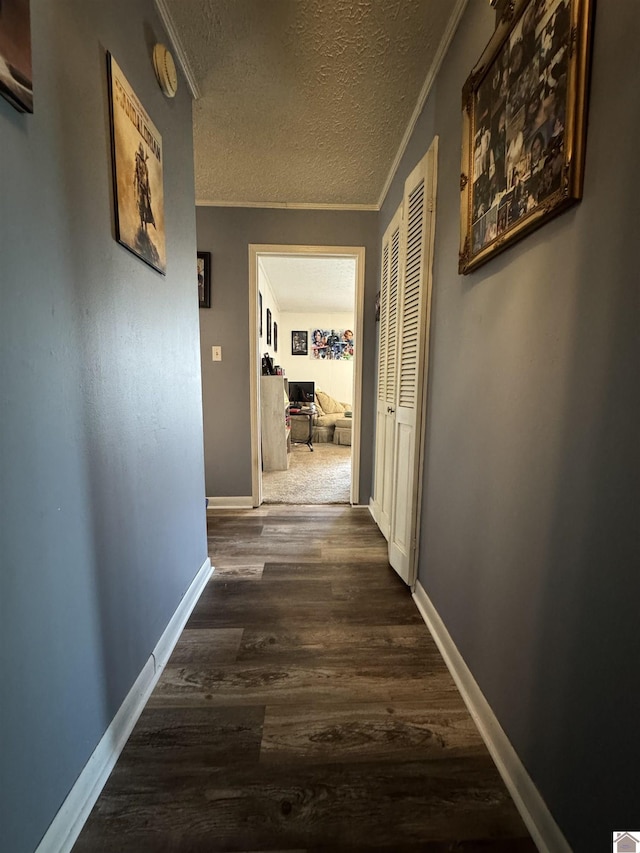 corridor with baseboards, crown molding, a textured ceiling, and wood finished floors