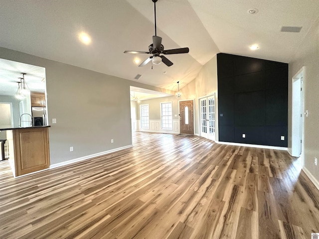 unfurnished living room with wood finished floors, a ceiling fan, baseboards, and high vaulted ceiling