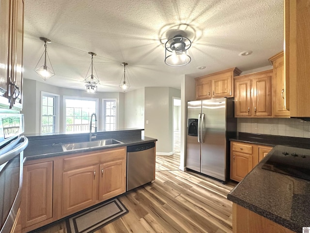 kitchen with stainless steel appliances, a sink, dark countertops, light wood-style flooring, and a textured ceiling