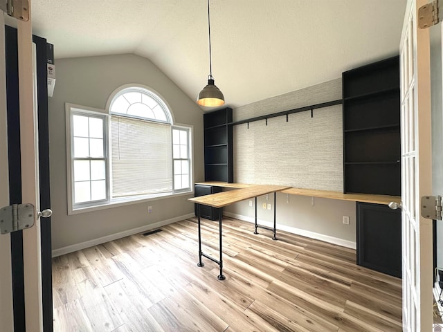 unfurnished office featuring vaulted ceiling, healthy amount of natural light, baseboards, wood finished floors, and a textured ceiling