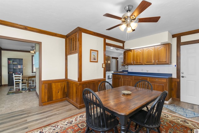 dining space featuring light wood-style flooring, wainscoting, a ceiling fan, and ornamental molding