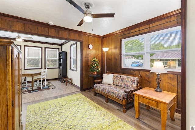 sitting room with a ceiling fan, ornamental molding, light wood-type flooring, wood walls, and baseboards