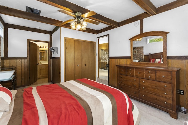 bedroom featuring a wainscoted wall, wood walls, carpet flooring, ensuite bath, and a ceiling fan