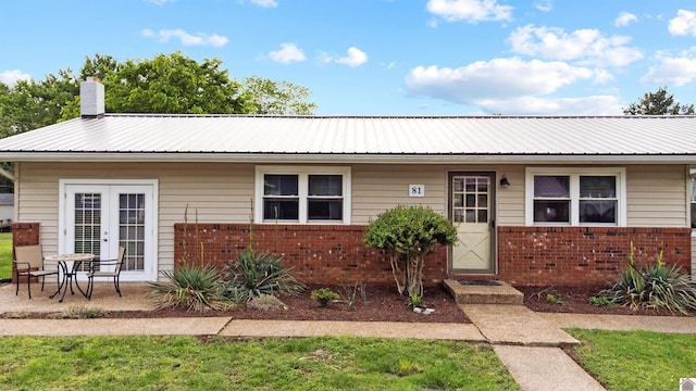 ranch-style house with brick siding, metal roof, a chimney, and french doors