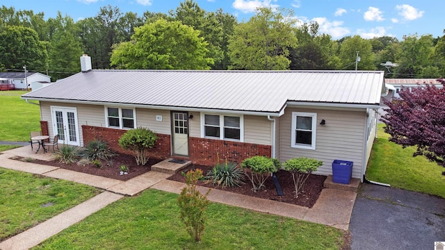 single story home with a front yard, brick siding, metal roof, and french doors