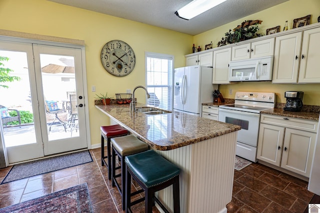 kitchen featuring white appliances, a sink, a breakfast bar, a peninsula, and white cabinetry