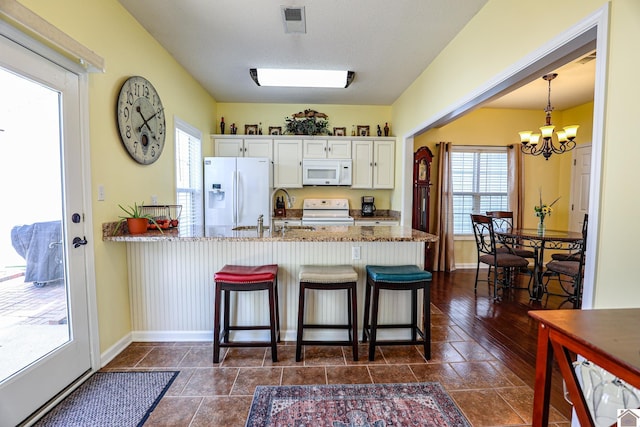 kitchen with white appliances, a sink, a peninsula, a chandelier, and baseboards
