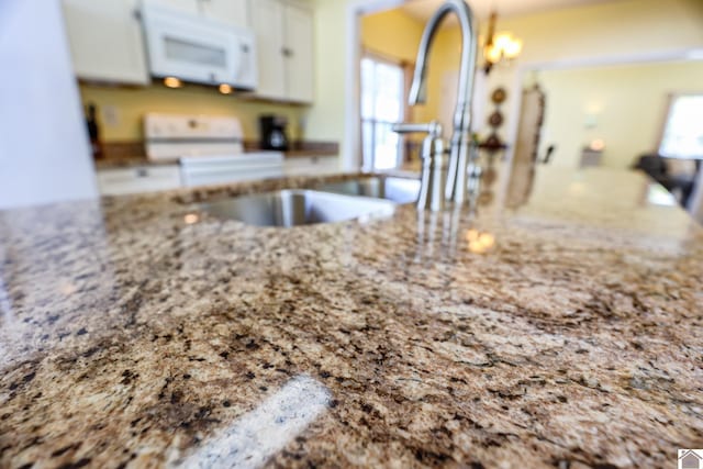 kitchen view of white microwave, white cabinets, light stone countertops, and stove