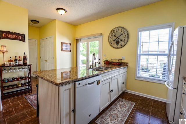 kitchen featuring a sink, white appliances, a peninsula, stone counters, and white cabinetry