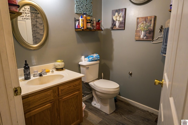 half bathroom with toilet, wood finished floors, vanity, and baseboards