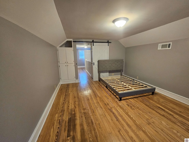 unfurnished bedroom with hardwood / wood-style floors, lofted ceiling, baseboards, and a barn door