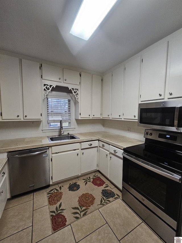 kitchen with appliances with stainless steel finishes, a sink, light tile patterned flooring, light countertops, and backsplash