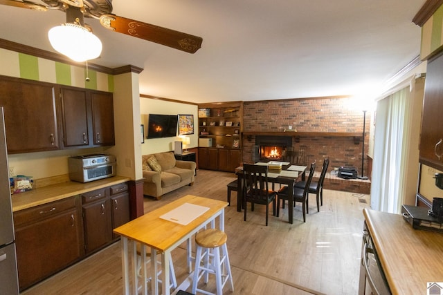 kitchen featuring dark brown cabinets, light wood-type flooring, a fireplace, light countertops, and brick wall