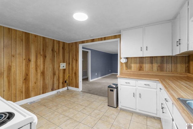 kitchen with wood walls, baseboards, white cabinets, light tile patterned flooring, and light colored carpet