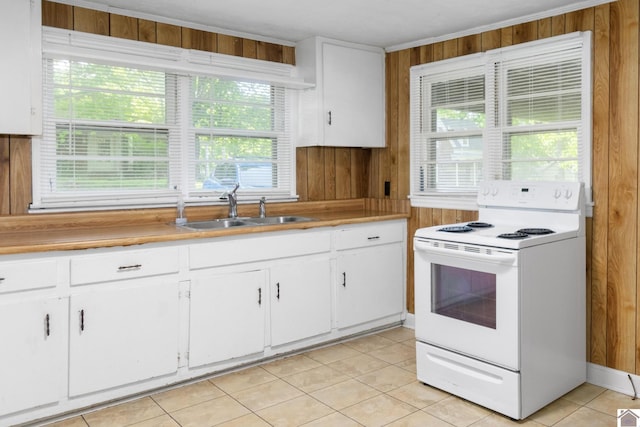 kitchen featuring white range with electric cooktop, a sink, wooden walls, healthy amount of natural light, and white cabinets