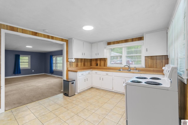 kitchen featuring white range with electric stovetop, light carpet, a sink, wood walls, and light countertops