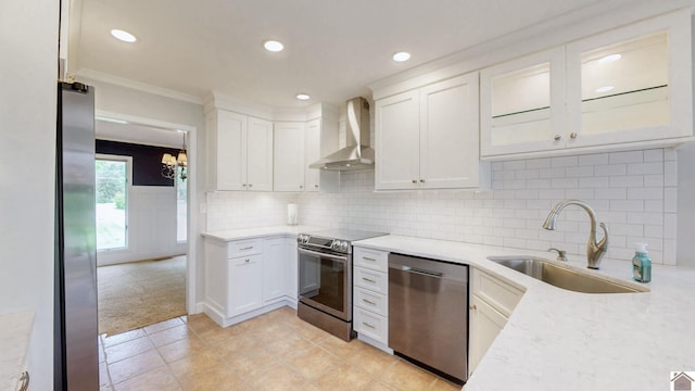 kitchen featuring wall chimney exhaust hood, stainless steel appliances, a sink, white cabinetry, and crown molding