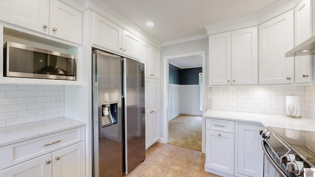 kitchen featuring appliances with stainless steel finishes, ornamental molding, white cabinets, light colored carpet, and light stone counters