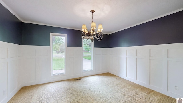 unfurnished dining area featuring a chandelier, a decorative wall, crown molding, light colored carpet, and a wainscoted wall