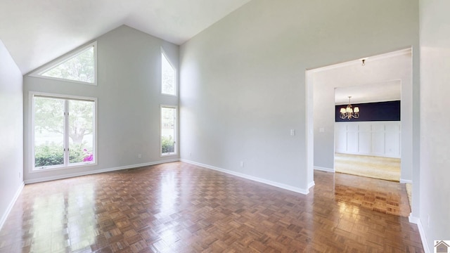 unfurnished living room with a chandelier, high vaulted ceiling, and baseboards